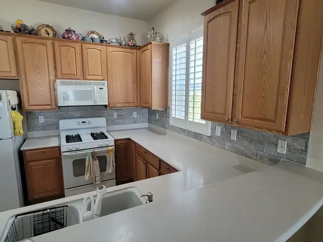 Oak kitchen with white counters and a gray stone-look plank tile backsplash under the cabinets
