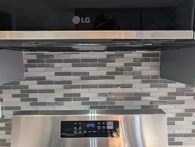 Gray and white glass mosaic backsplash installed between a stainless range and an over-the-range microwave, a job for a veteran family