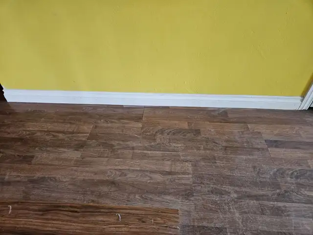 Wood-look plank tile floor with white baseboard along a yellow wall