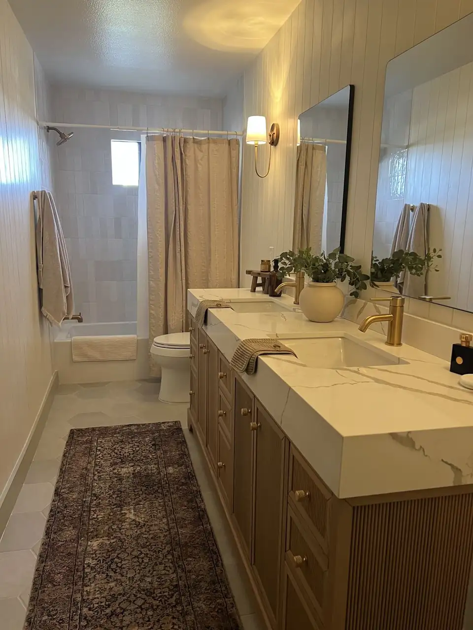 Guest bathroom tiled by Veteran Tile Works, a tile contractor in Beaumont: stacked white tile tub surround, light gray hexagon floor tile and a fluted wood double vanity with a marble-look top and brass faucets