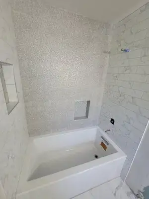 Tub surround with white marble-look subway tile, a shimmering mosaic accent wall and two recessed shampoo niches